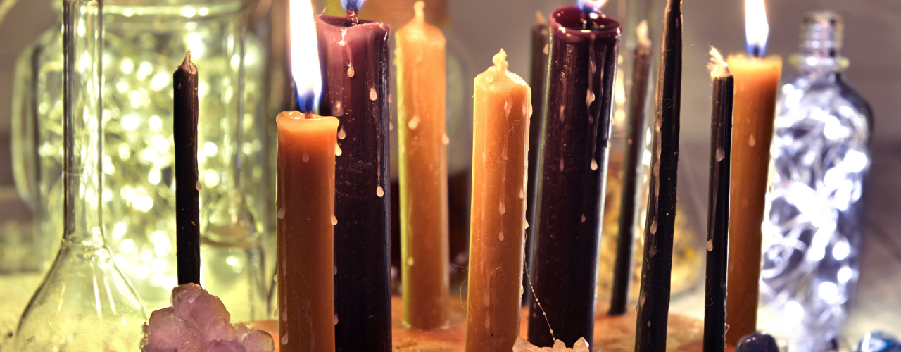 Conjunto de velas altas em tons variados — preto, bordeaux e bege — com cristais, usadas em ritual de magia natural