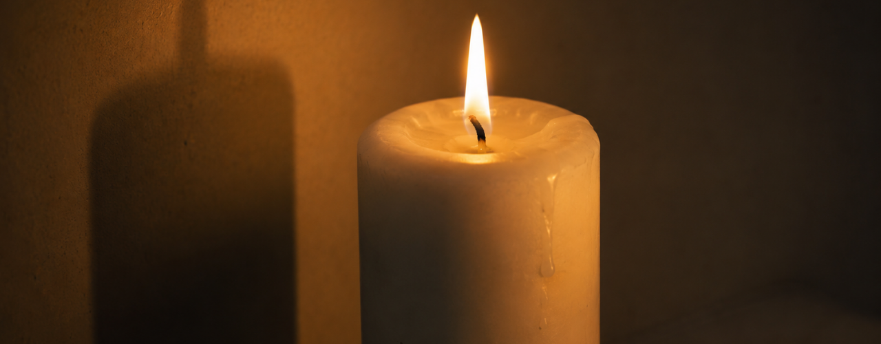 Vela branca acesa sobre fundo escuro, com luz e sombra em equilíbrio, simbolizando a neutralidade da magia natural