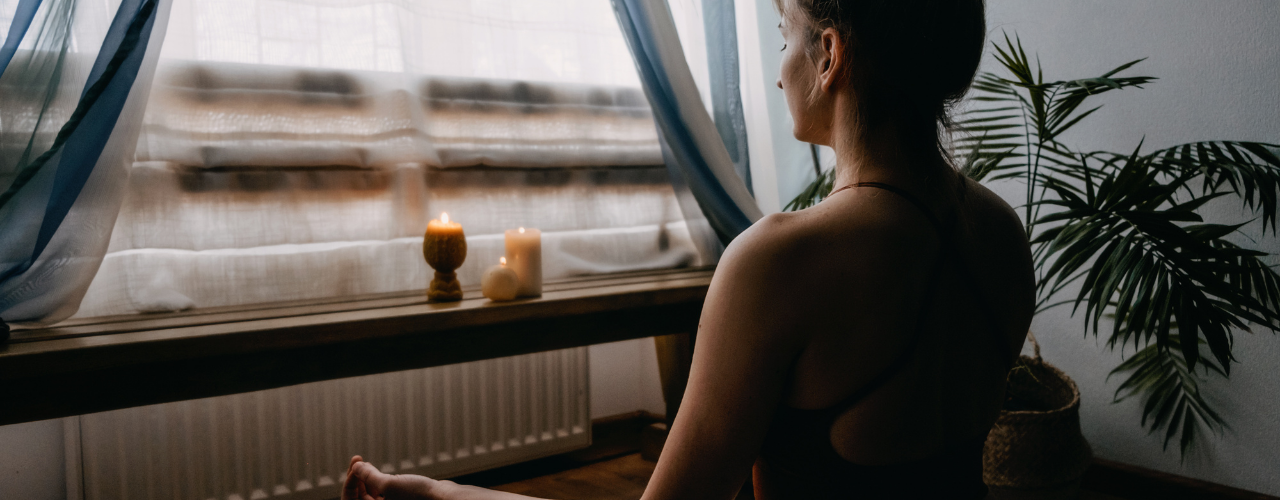 Mulher em meditação junto à janela com velas — práticas de proteção energética para fazer antes de sair de casa