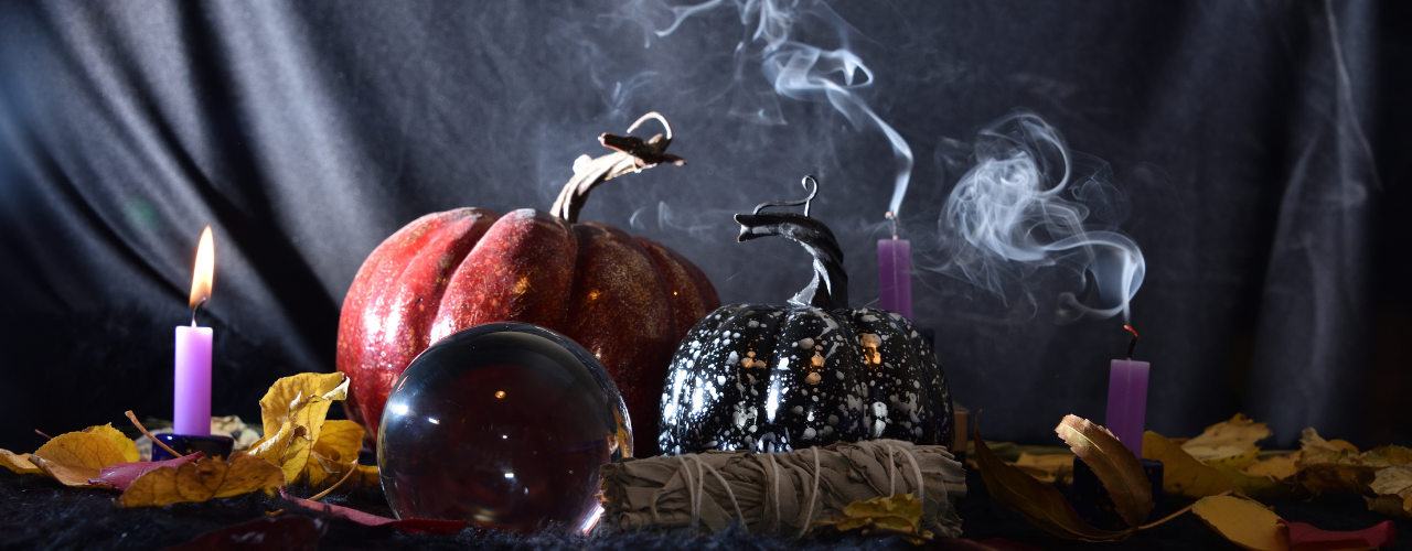 Mesa de ritual de Samhain com abóboras, velas roxas, esfera de cristal e fumo de defumação