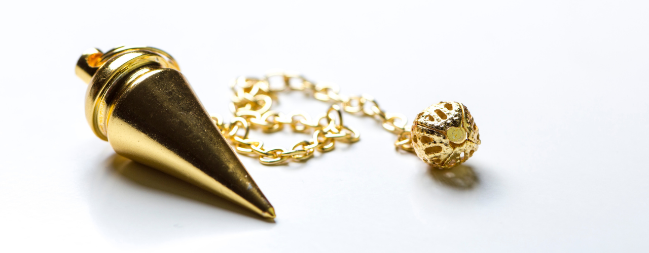 Pêndulo dourado pousado e imóvel sobre superfície clara, simbolizando silêncio interior e momentos em que o pêndulo não responde.