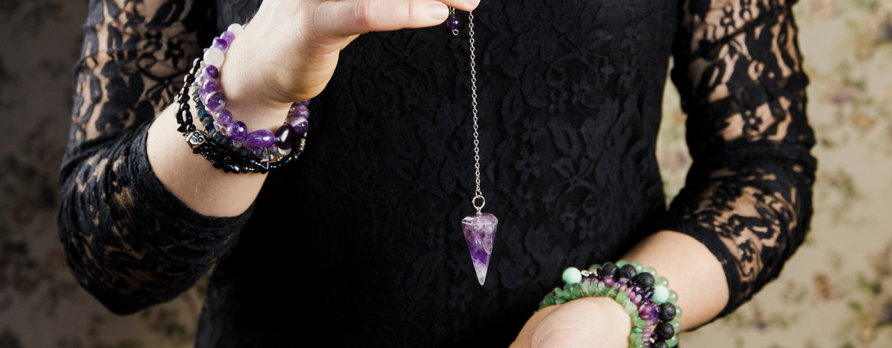 Mão a segurar um pêndulo de cristal violeta, momento de clareza intuitiva antes de uma decisão difícil