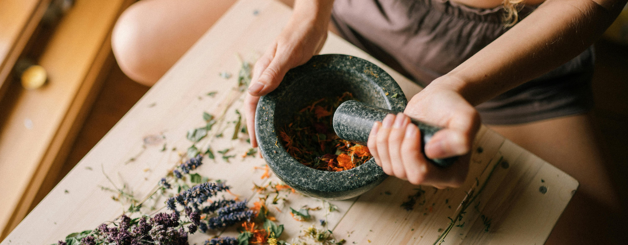 Mãos a preparar ervas aromáticas num almofariz para banho de limpeza energética